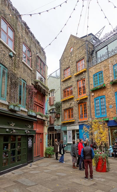 A group of people standing in a small urban outdoor courtyard surrounded by multi-storey buildings with colorful window frames in shades of blue, orange, and green. The buildings have brick facades, s