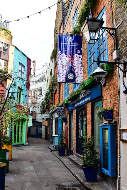 A view of a narrow courtyard in Covent Garden surrounded by multi-story brick buildings with brightly painted window frames in orange, blue, and green. The buildings feature small balconies and weathe